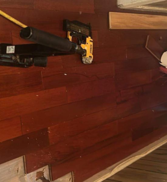 A man uses a nail gun to work on a wooden floor, showcasing construction expertise in a remodeling project.