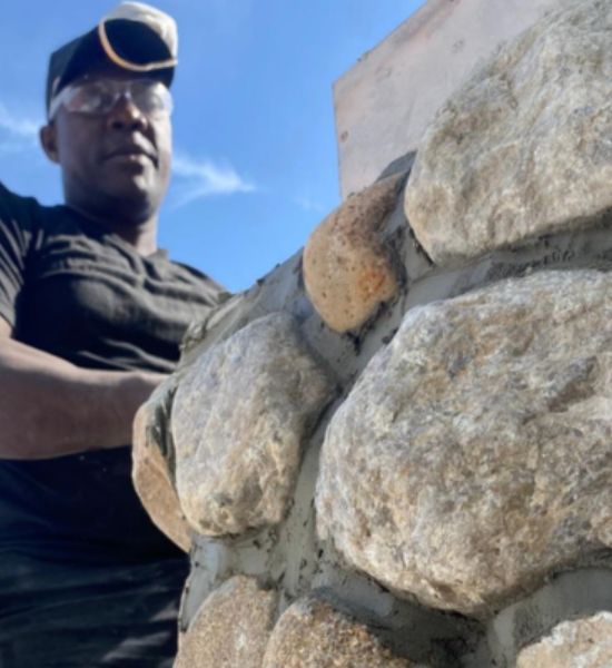 A man diligently constructs a stone wall, showcasing expertise in building design and general contracting services.