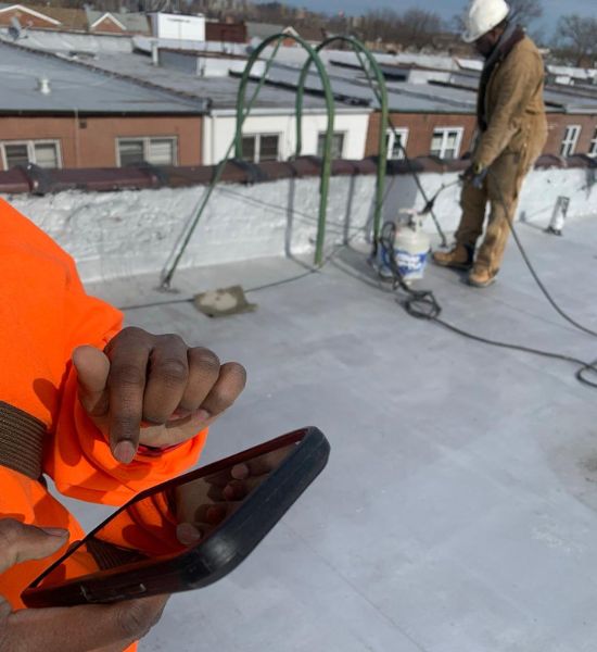 A man in an orange shirt is engaged with a cell phone, representing modern communication in the construction industry.