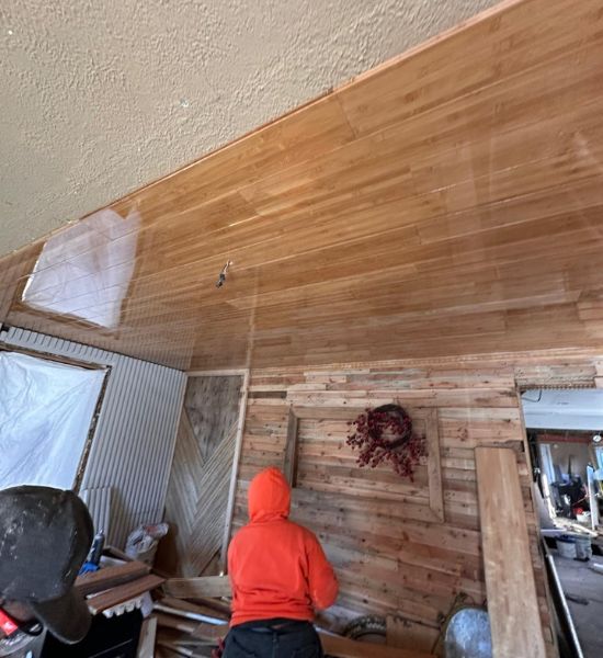 A man meticulously works on a wooden ceiling, showcasing craftsmanship in a residential remodeling project by Greater Mansion.