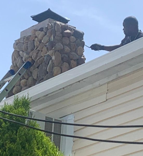 A man performs chimney work on a house, showcasing expertise in construction and remodeling services by Greater Mansion.