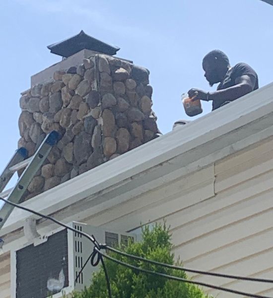 A worker is engaged in chimney maintenance on a rooftop, highlighting skills in roofing and general contracting.