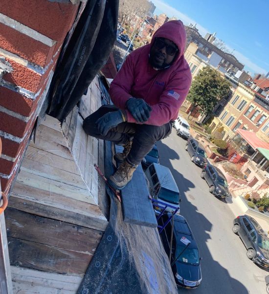 A man in a pink hoodie diligently works on a roof, showcasing expertise in roofing services for Greater Mansion.