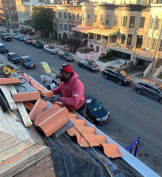 A man performs roofing work on a red roof, showcasing expertise in construction and remodeling services.