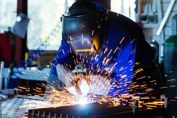 A man welding metal in a factory setting, showcasing skilled craftsmanship in construction and remodeling services.