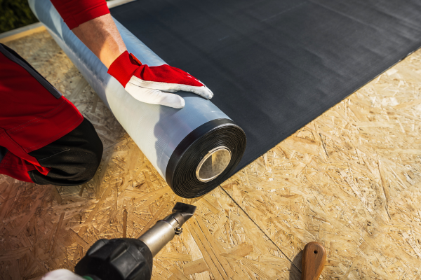 A man operates a drill to install black plastic, showcasing construction work by Greater Mansion in Brooklyn, NY.