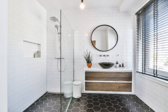 A stylish bathroom featuring black and white tiles, complemented by a round mirror, showcasing modern design elements.