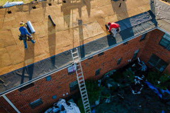 Two workers on a roof with a ladder, showcasing Greater Mansion's roofing services in Brooklyn's construction industry.