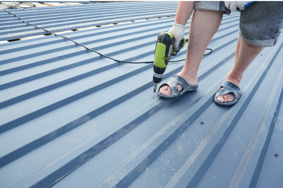 A person repairs a metal roof using a drill, showcasing construction work by Greater Mansion in Brooklyn.