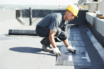 A man in a hard hat and safety vest works on a roof, showcasing construction expertise in Brooklyn by Greater Mansion.