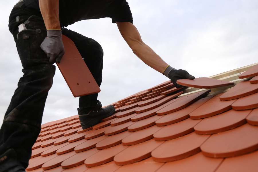 A man installs a red tile on a roof, showcasing skilled craftsmanship in roofing for Greater Mansion in Brooklyn.