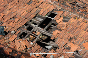 A man stands on a destroyed roof, symbolizing the need for expert construction and remodeling services in Brooklyn.