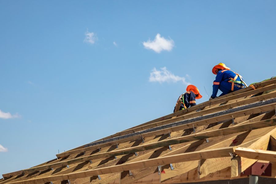 Two men working on a roof under a clear blue sky, representing Greater Mansion's construction services in Brooklyn.