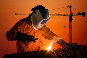 A welder in an orange suit skillfully welding steel, showcasing expertise in construction and welding services.